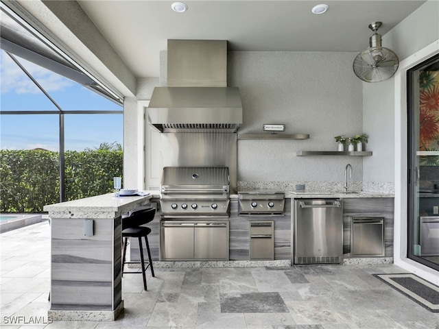 view of patio featuring exterior kitchen, glass enclosure, a grill, ceiling fan, and an outdoor wet bar