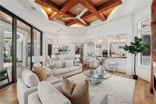 living room with a towering ceiling, coffered ceiling, a notable chandelier, light hardwood / wood-style floors, and beam ceiling