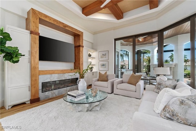 living room with coffered ceiling, crown molding, light wood-type flooring, a high end fireplace, and beam ceiling