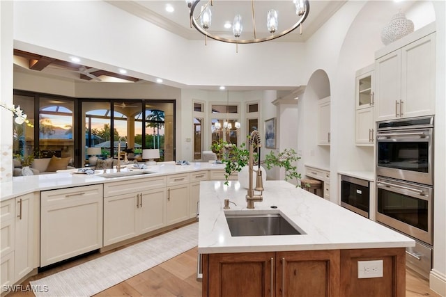 kitchen with white dishwasher, double oven, decorative light fixtures, and a center island with sink