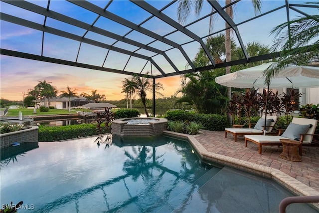 pool at dusk with an in ground hot tub, glass enclosure, and a patio