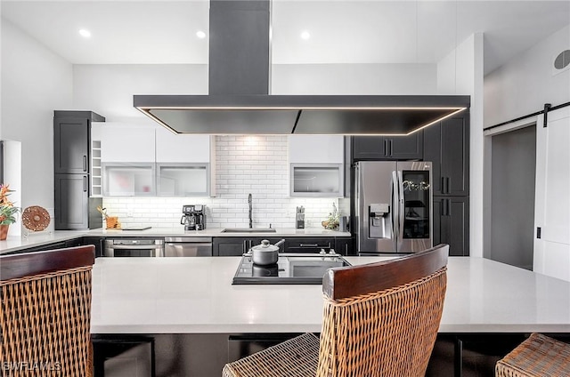 kitchen with a barn door, decorative backsplash, stainless steel fridge, and island exhaust hood