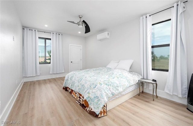 bedroom with ceiling fan, a wall unit AC, and light wood-type flooring