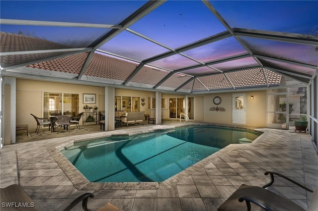 pool at dusk with glass enclosure, a patio area, and outdoor lounge area