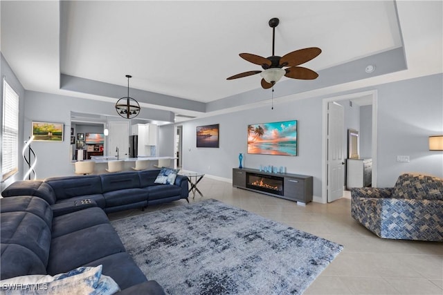 tiled living room with ceiling fan with notable chandelier and a raised ceiling