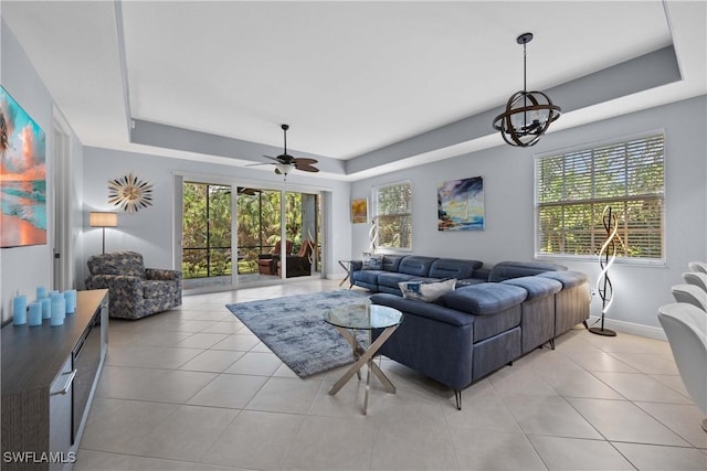 tiled living room featuring ceiling fan with notable chandelier and a raised ceiling