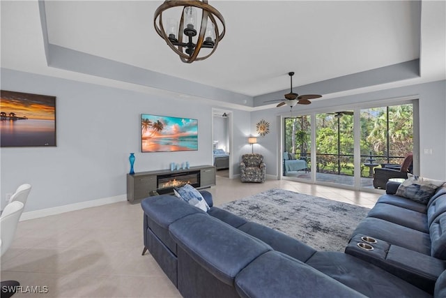 tiled living room with a raised ceiling and ceiling fan with notable chandelier