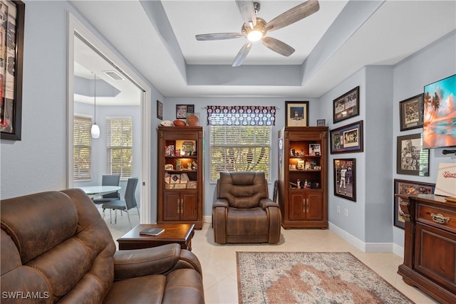 living area with ceiling fan, light tile patterned flooring, and a tray ceiling