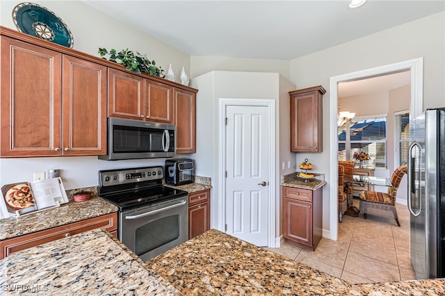 kitchen featuring light stone counters, appliances with stainless steel finishes, a notable chandelier, and light tile patterned flooring