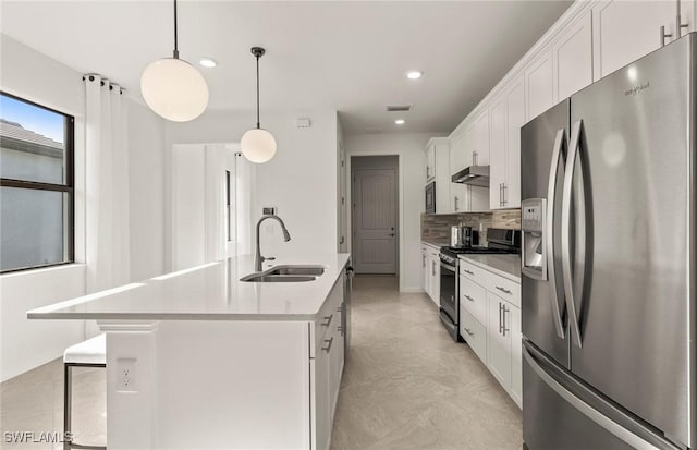 kitchen with an island with sink, appliances with stainless steel finishes, pendant lighting, white cabinets, and sink