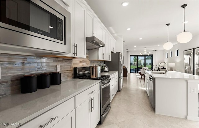 kitchen featuring white cabinets, appliances with stainless steel finishes, decorative light fixtures, decorative backsplash, and a center island with sink