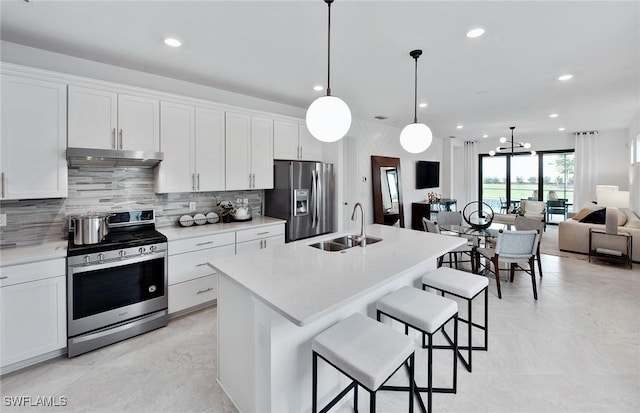 kitchen featuring decorative light fixtures, a center island with sink, sink, stainless steel appliances, and white cabinets