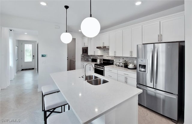 kitchen with white cabinets, appliances with stainless steel finishes, sink, hanging light fixtures, and a center island with sink