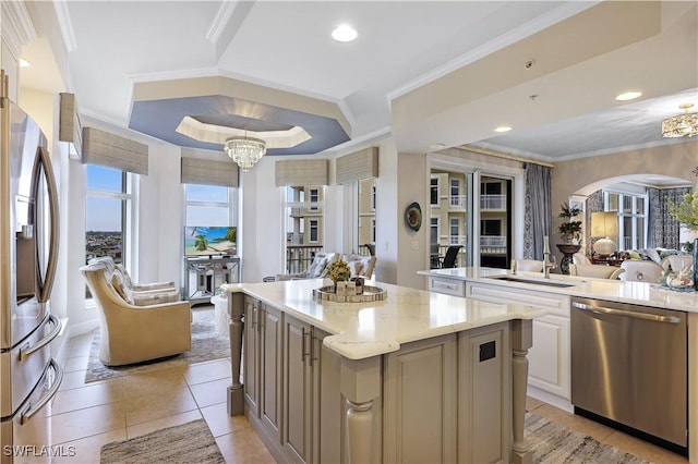 kitchen with a kitchen island, a tray ceiling, appliances with stainless steel finishes, ornamental molding, and light stone counters