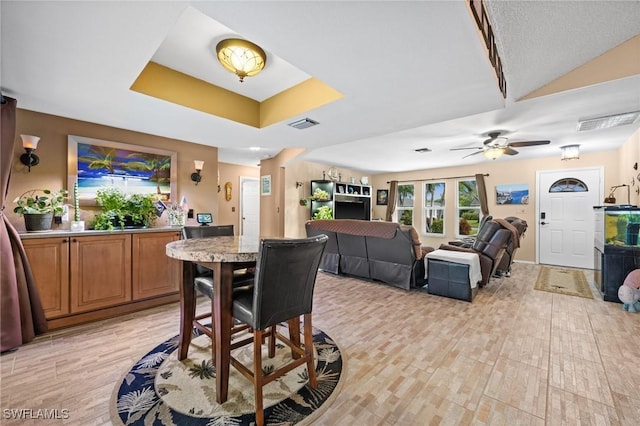 dining room with light hardwood / wood-style floors, a tray ceiling, and ceiling fan