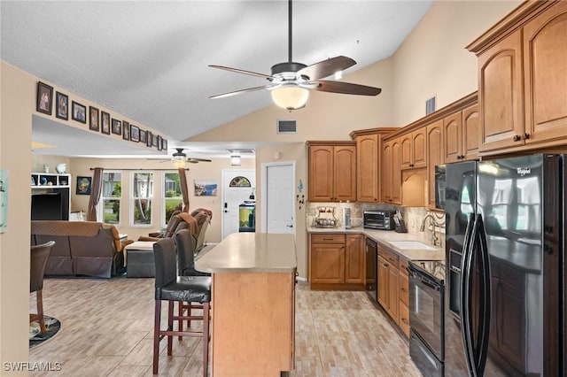 kitchen featuring black appliances, lofted ceiling, a kitchen island, sink, and a breakfast bar area