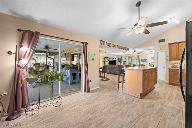 kitchen featuring lofted ceiling, a kitchen island, black refrigerator, light wood-type flooring, and a breakfast bar area