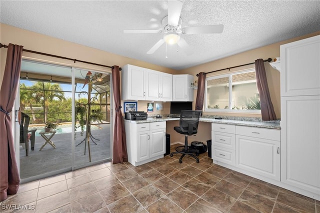 unfurnished office featuring ceiling fan, a textured ceiling, built in desk, and a healthy amount of sunlight