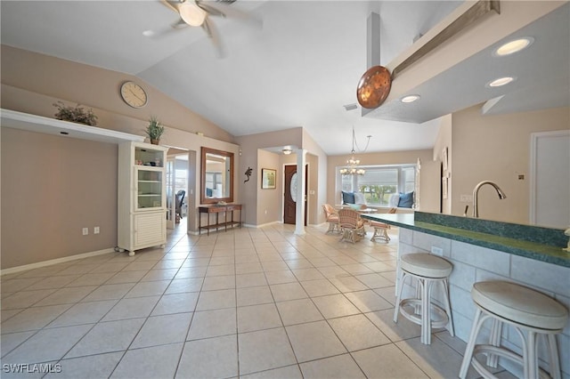 kitchen featuring light tile patterned floors, ceiling fan with notable chandelier, a breakfast bar, and vaulted ceiling