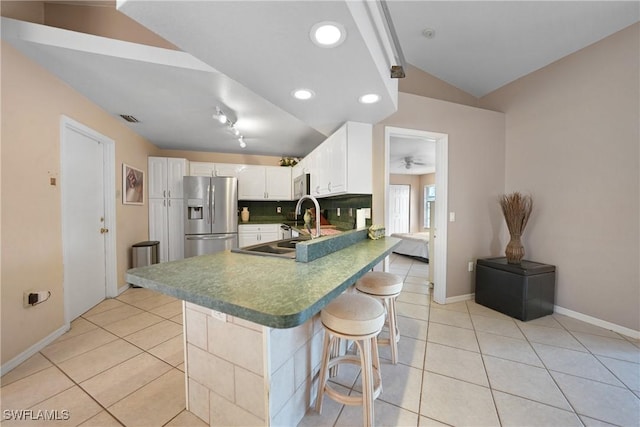 kitchen with white cabinetry, stainless steel appliances, backsplash, vaulted ceiling, and a breakfast bar