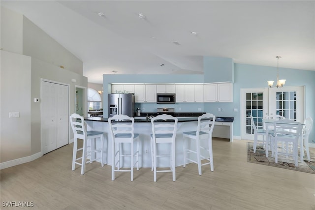 kitchen featuring white cabinetry, hanging light fixtures, stainless steel appliances, a notable chandelier, and an island with sink