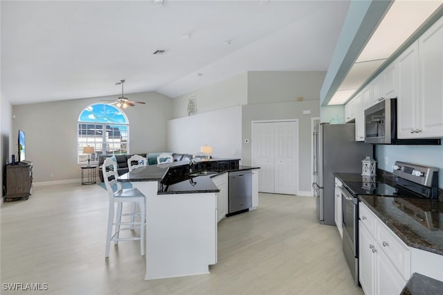 kitchen featuring vaulted ceiling, appliances with stainless steel finishes, sink, white cabinets, and dark stone counters