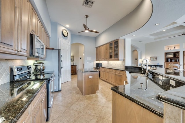 kitchen featuring ceiling fan, stainless steel appliances, sink, dark stone counters, and a center island