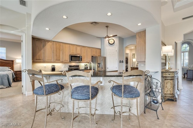 kitchen with a kitchen bar, stainless steel appliances, backsplash, kitchen peninsula, and ornamental molding