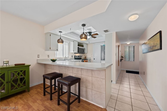 kitchen with appliances with stainless steel finishes, a kitchen breakfast bar, white cabinets, light tile patterned floors, and kitchen peninsula