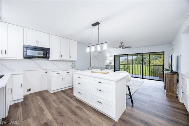 kitchen with a breakfast bar area, white cabinetry, a center island, hanging light fixtures, and backsplash