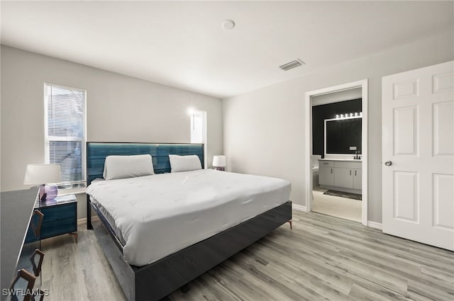 bedroom with ensuite bathroom and light wood-type flooring