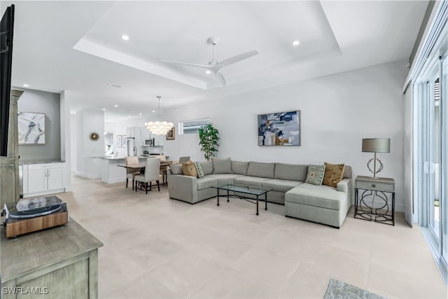 living room with a raised ceiling, light tile patterned floors, and ceiling fan with notable chandelier