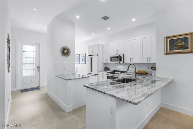 kitchen with light stone countertops, white cabinetry, sink, kitchen peninsula, and high quality appliances