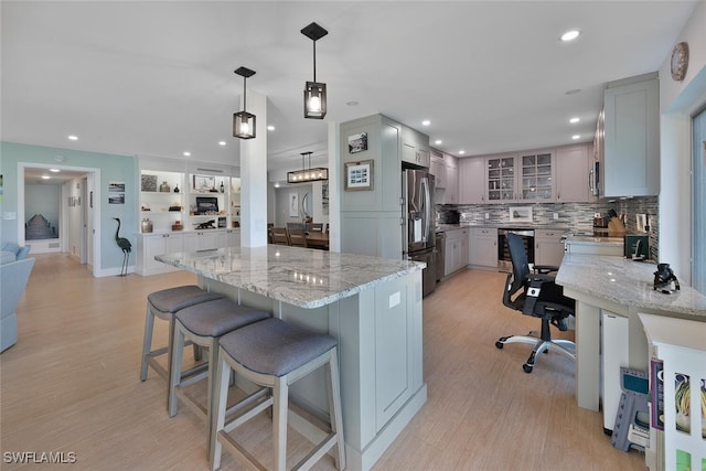 kitchen featuring gray cabinets, light stone counters, hanging light fixtures, and stainless steel appliances