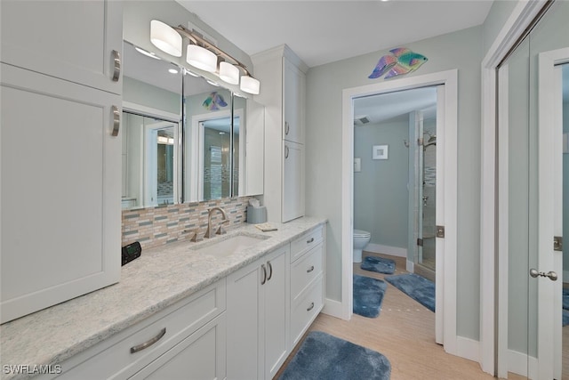 bathroom featuring hardwood / wood-style floors, a shower with door, vanity, backsplash, and toilet