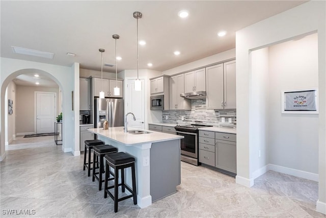 kitchen with pendant lighting, stainless steel appliances, gray cabinets, and an island with sink