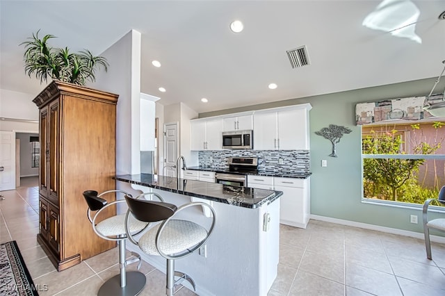 kitchen with kitchen peninsula, decorative backsplash, white cabinetry, a breakfast bar area, and stainless steel appliances