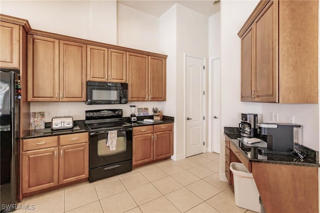 kitchen featuring black appliances, light tile patterned floors, dark stone counters, and a high ceiling