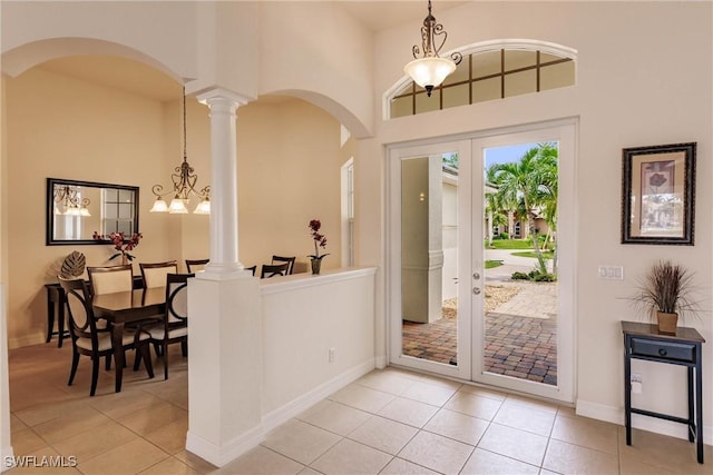 tiled foyer entrance featuring decorative columns, a high ceiling, french doors, and an inviting chandelier