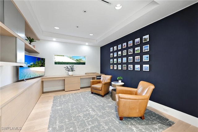 living area featuring a raised ceiling, light hardwood / wood-style flooring, and built in desk