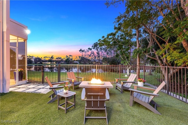 patio terrace at dusk featuring a water view, an outdoor fire pit, and a lawn