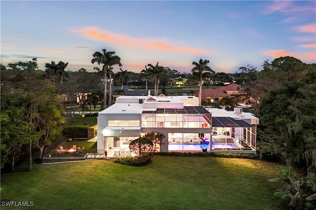 back house at dusk with a balcony and a yard