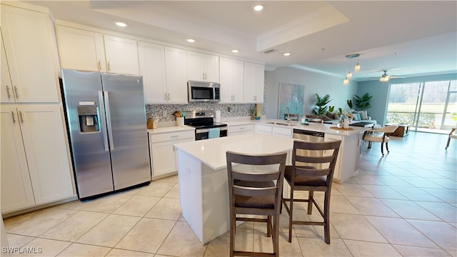 kitchen featuring kitchen peninsula, sink, a tray ceiling, appliances with stainless steel finishes, and a breakfast bar area