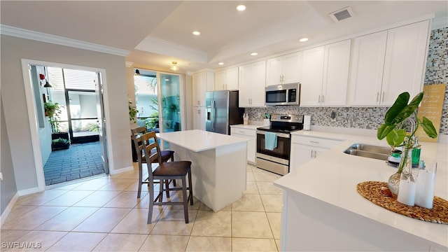 kitchen with white cabinets, a kitchen island, stainless steel appliances, backsplash, and a breakfast bar