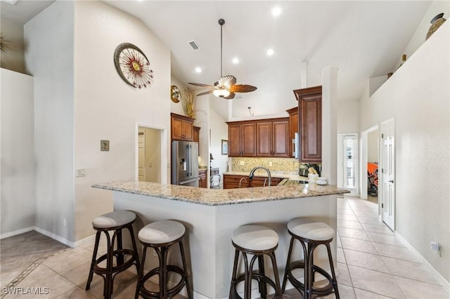 kitchen featuring light tile patterned floors, stainless steel fridge, ceiling fan, light stone countertops, and decorative backsplash