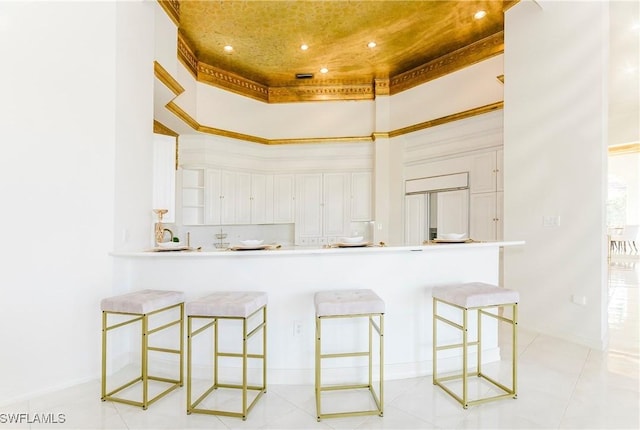 kitchen featuring white cabinets, a towering ceiling, a kitchen breakfast bar, kitchen peninsula, and a tray ceiling