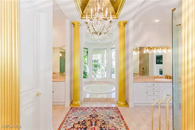 bathroom featuring tiled bath, vanity, a notable chandelier, a raised ceiling, and ornate columns