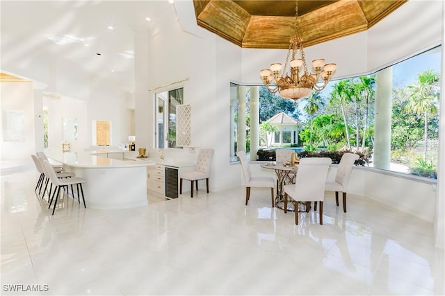 dining space featuring a towering ceiling, beverage cooler, and a chandelier