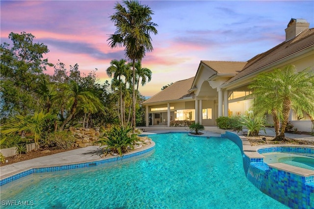 pool at dusk featuring an in ground hot tub