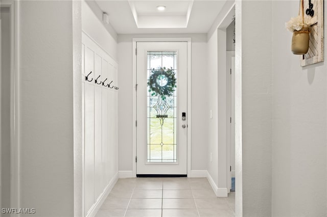 doorway with a raised ceiling and light tile patterned flooring